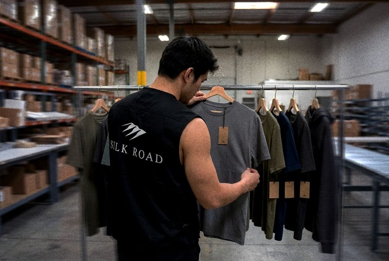 A Silk Road staff member checking sample garments hanging on a rail with hangtags in a warehouse