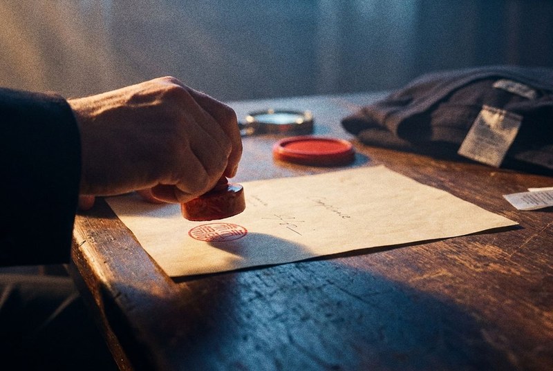 A hand pressing a red chop seal onto a document, beside a folded garment and its care labels